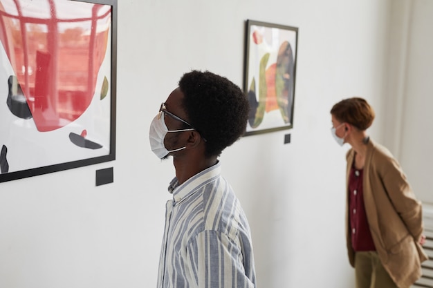 Ritratto di due giovani che guardano i dipinti mentre indossano maschere alla mostra della galleria d'arte moderna,