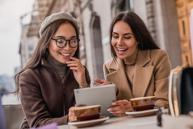 Ritratto di due giovani donne sorridenti al tavolo di un bar guardando in tavoletta digitale