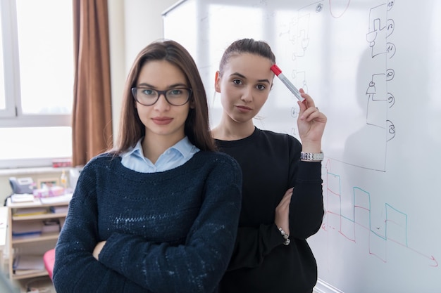 ritratto di due giovani studentesse in piedi davanti a una lavagna bianca e guardando la telecamera