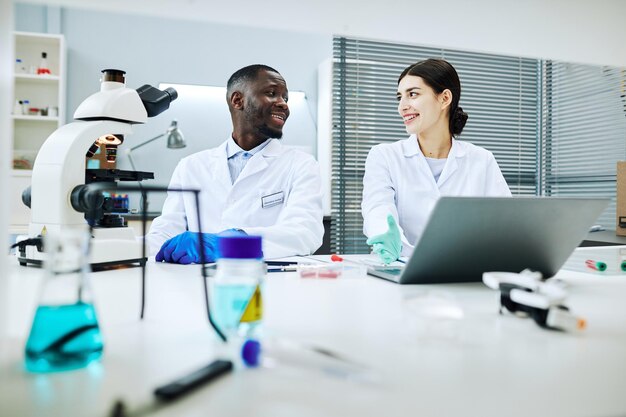 Ritratto di due lavoratori di laboratorio sorridenti che si guardano l'un l'altro mentre fanno ricerche mediche