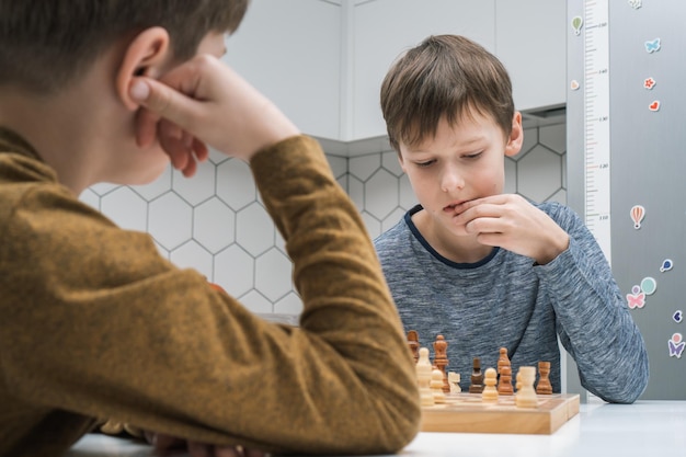 Ritratto di due ragazzi concentrati del preteen che si siedono al tavolo che giocano a scacchi sulla strategia di edificio di pensiero del bordo di legno