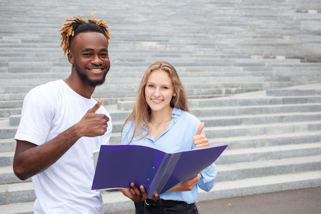 Ritratto di due studenti multietnici sorridenti con facce fortunate in posa all'aperto