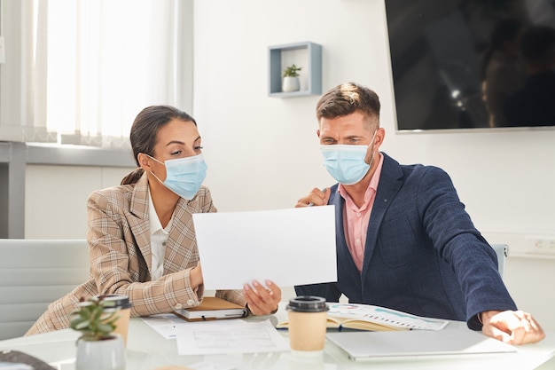 Ritratto di due uomini d'affari uomo e donna che indossa maschere guardando i documenti durante la riunione presso l'ufficio post pandemia