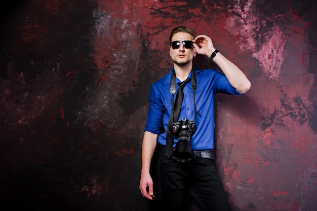 ritratto di elegante fotografo professionista uomo con la macchina fotografica, indossare camicia e cravatta blu, occhiali da sole.