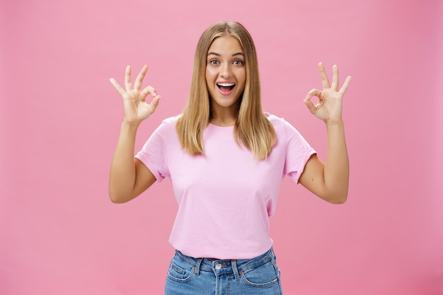 Ritratto di entusiasta attraente ragazza caucasica in t-shirt alla moda e jeans che mostrano bene o confermare il gesto con un ampio sorriso divertito in piedi soddisfatto reagendo a ottime notizie