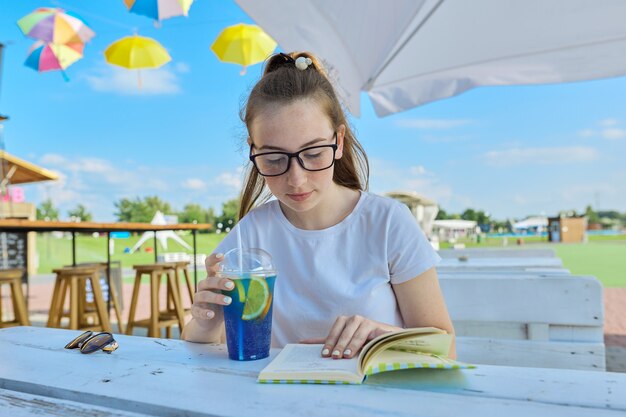 Ritratto di estate dell'adolescente in vetri che leggono il libro