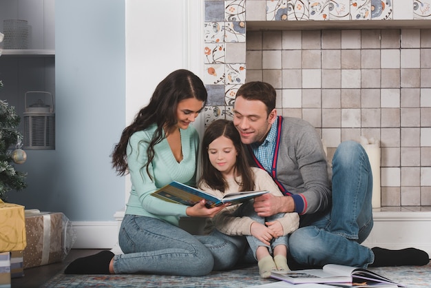 Ritratto di famiglia di genitori felici e della loro figlia che leggono insieme a casa