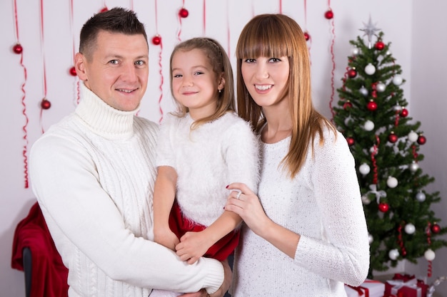 Ritratto di famiglia di genitori felici e figlia con albero di Natale decorato