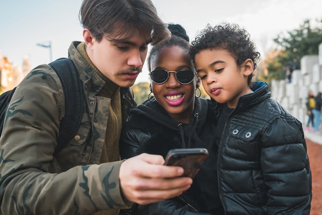 Ritratto di famiglia etnica bella razza mista divertendosi, rilassarsi e utilizzando il telefono cellulare presso il parco all'aperto.