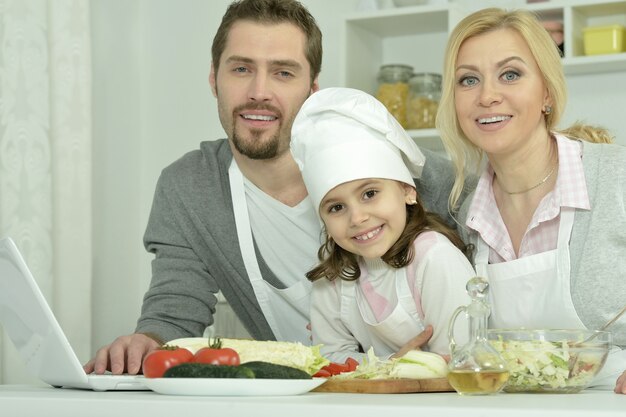 Ritratto di famiglia felice che cucina in cucina con laptop