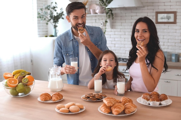 Ritratto di famiglia felice che mangia biscotti con latte e guarda la telecamera