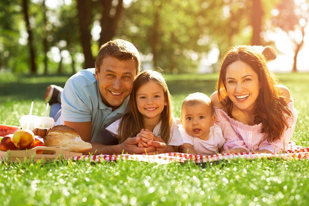 Ritratto di famiglia felice con due bambini sdraiati sulla coperta nel parco e guardando la telecamera