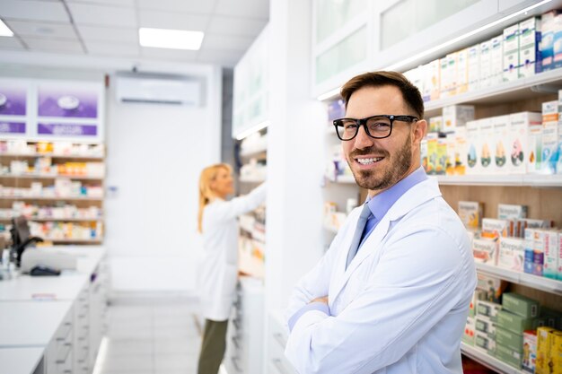 Ritratto di farmacista caucasico sorridente in piedi in negozio di droga con le braccia incrociate.