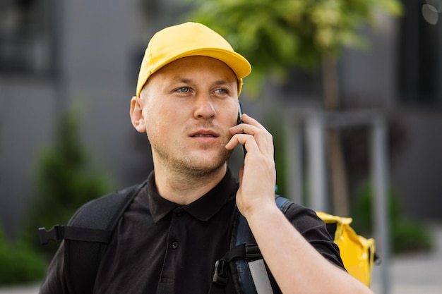 Ritratto di fattorino in berretto giallo con zaino termico che controlla gli ordini tramite smartphone