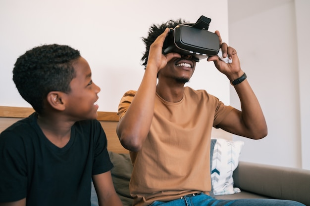 Ritratto di felice afroamericano padre e figlio seduti nel divano e giocare ai videogiochi con gli occhiali Vr insieme a casa