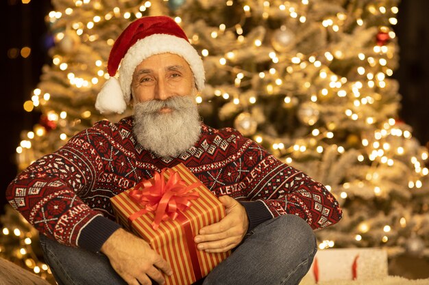 Ritratto di felice Babbo Natale seduto nella sua stanza a casa vicino all'albero di Natale.