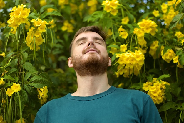 Ritratto di felice bel ragazzo barbuto giovane uomo positivo con la barba sta sentendo l'odore di un bel giallo