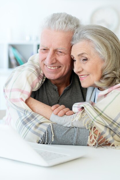 Ritratto di felice bella coppia senior con coperta utilizzando il computer portatile a casa