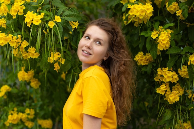 Ritratto di felice bella ragazza barbuta giovane donna positiva con la barba sta annusando bellissimi fiori gialli nel giardino sorridendo godendosi la primavera o la giornata estiva respirando aria profondamente fresca