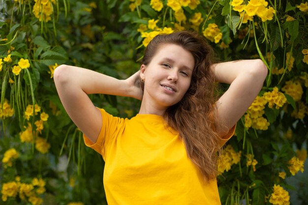 Ritratto di felice bella ragazza barbuta giovane donna positiva con la barba sta annusando bellissimi fiori gialli nel giardino sorridendo godendosi la primavera o la giornata estiva respirando aria profondamente fresca