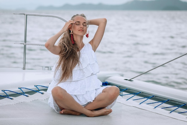 Ritratto di felice bella ragazza con abito bianco e lunghi capelli biondi ricci seduto su yacht in estate. guardando la fotocamera con un sorriso a trentadue denti.