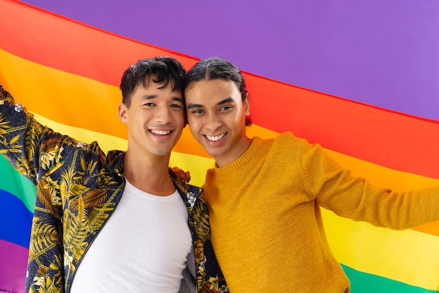 Ritratto di felice coppia maschile birazziale che abbraccia e tiene bandiera lgbt su sfondo viola. Concetto lgbt e orgoglio.