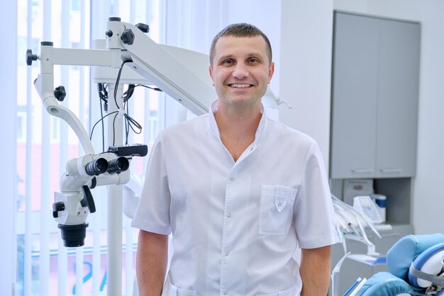 Ritratto di felice dentista maschio amichevole, medico professionista sorridente che guarda l'obbiettivo in clinica dentale