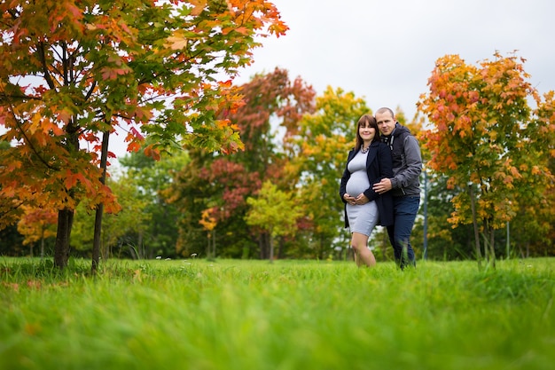 Ritratto di felice donna incinta e suo marito in posa in autunno park