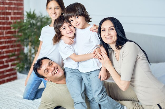 Ritratto di felice famiglia latina, genitori e bambini che sorridono alla telecamera mentre trascorrono del tempo insieme a casa. Infanzia felice, concetto di genitorialità