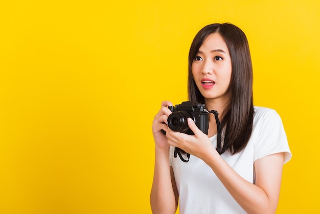 Ritratto di felice fotografo asiatico bella giovane donna che tiene la fotocamera digitale vintage mirrorless sulle mani, studio girato isolato su sfondo giallo, stile di vita adolescente concetto di viaggio hobby