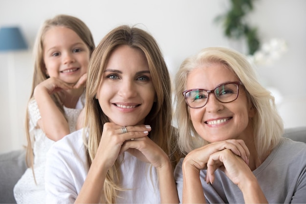 Ritratto di felice generazione di tre donne nonna mamma e nipote bambino che si tengono per mano sotto il mento guardando la fotocamera giovane figlia adulta sorridente nonna anziana e bambino ragazza famiglia primo piano del volto