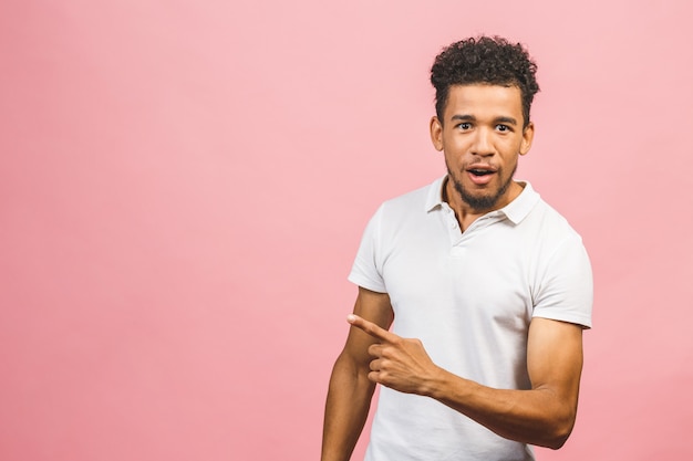 Ritratto di felice giovane bello studente maschio dalla pelle abbronzata con acconciatura afro nel sorridere casuale, che indica da parte con il dito, guardando a porte chiuse con espressione faccia eccitata