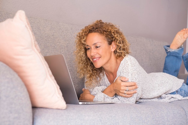 Ritratto di felice giovane donna adulta che utilizza il computer sdraiata sul divano a casa in attività di relax al coperto per il tempo libero da sola Persone che lavorano come freelance a proprio agio sul divano Navigando in rete sui social