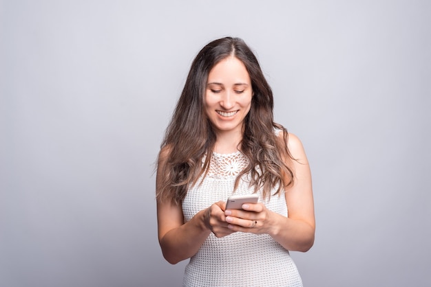 Ritratto di felice giovane donna in piedi sul muro bianco e utilizzando il telefono.