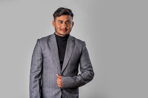 Ritratto di felice indiano giovane uomo d'affari che indossa un blazer su sfondo grigio in posa soddisfatto maschio di successo in abito formale