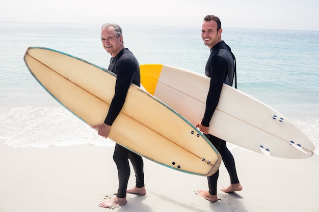 Ritratto di felice padre e figlio in muta tenendo una tavola da surf