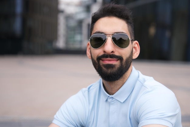 Ritratto di felice positivo ragazzo etnico arabo musulmano giovane con barba nera in occhiali da sole sorridente