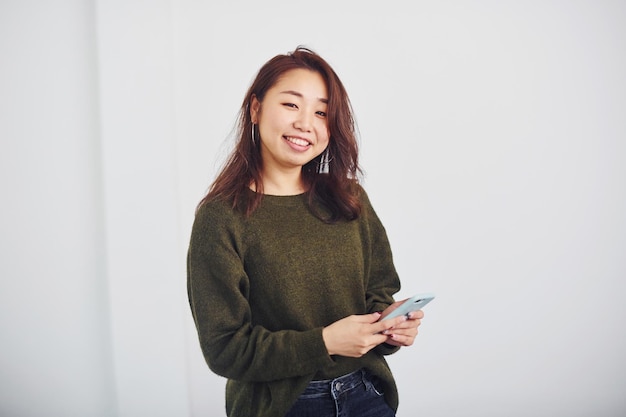 Ritratto di felice ragazza asiatica che sta al chiuso in studio su sfondo bianco.