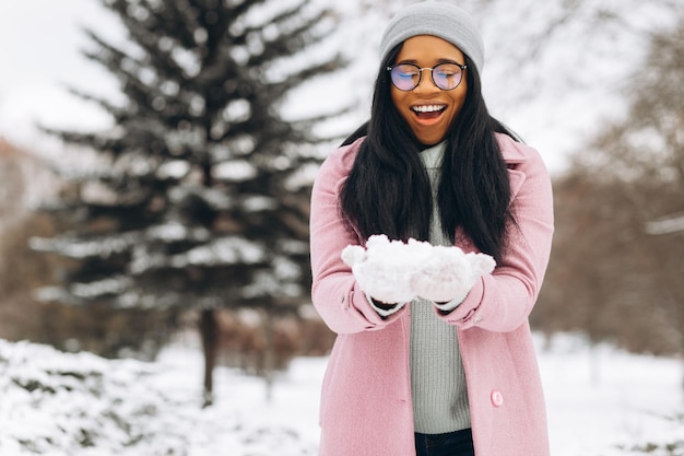 Ritratto di felice ragazza positiva Giovane donna afroamericana in occhiali e guanti nel parco invernale