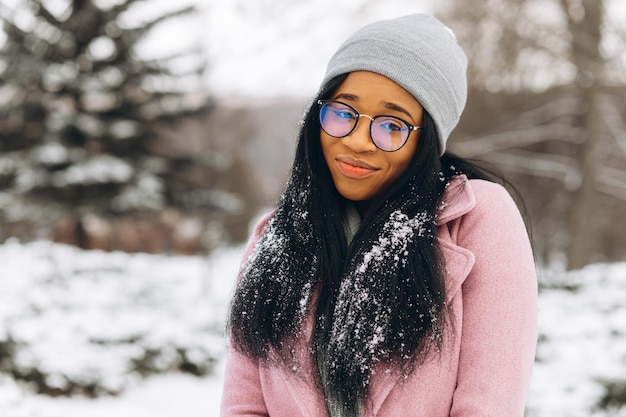 Ritratto di felice ragazza positiva Giovane donna afroamericana in occhiali e guanti nel parco invernale