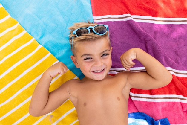 Ritratto di felice ragazzo biraziale sorridente e sdraiato sull'asciugamano a bordo piscina. Trascorrere tempo di qualità, stile di vita, infanzia, estate e concetto di vacanza.