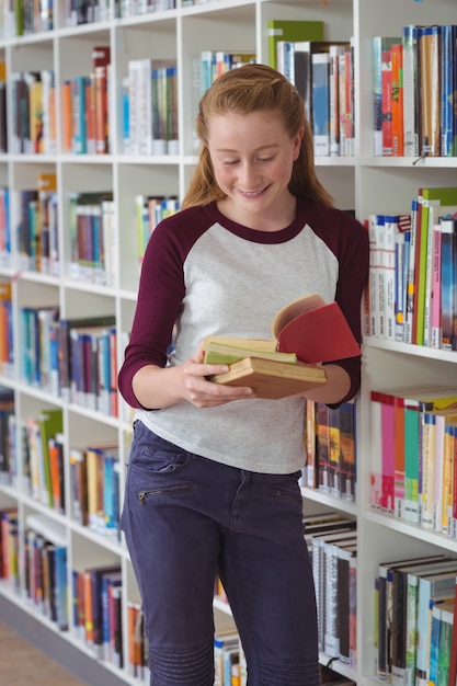 Ritratto di felice scolara leggendo libri in biblioteca