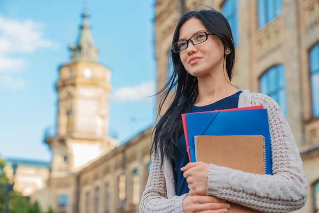 Ritratto di felice studentessa che tiene libri e distoglie lo sguardo all'aperto