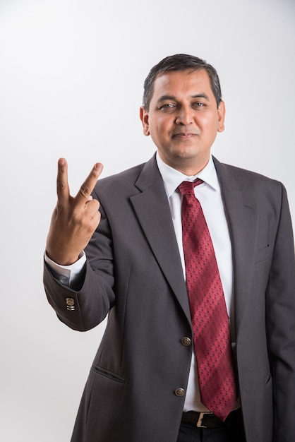 Ritratto di felice uomo d'affari indiano o asiatico di mezza età in abito nero con segno di successo mentre in piedi isolato su sfondo bianco