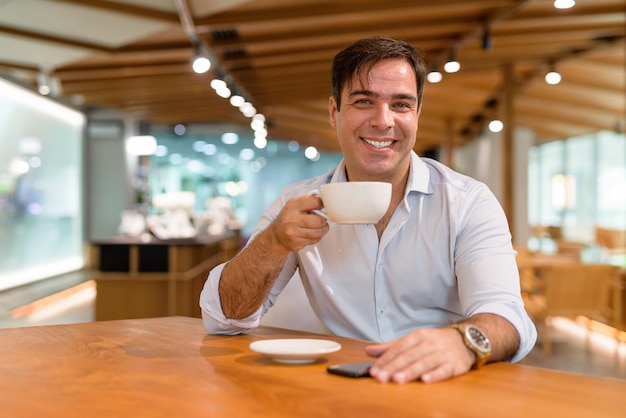 Ritratto di felice uomo persiano seduto e sorridente al coffee shop