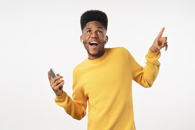 Ritratto di felice uomo vestito casual con auricolari che ballano mentre si ascolta musica sullo smartphone