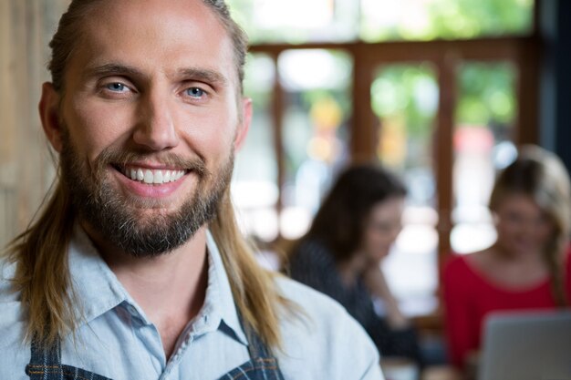 Ritratto di fiducioso barista maschio con clienti di sesso femminile in background presso la caffetteria