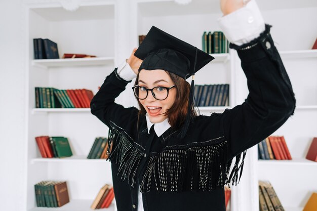 Ritratto di fiducioso giovane studentessa caucasica in libreria per celebrare la laurea