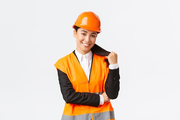 Ritratto di fiducioso sorridente manager edile donna asiatica, ingegnere nell'area di costruzione, indossando casco di sicurezza e giacca riflettente che sembra felice del progetto, soddisfatto del lavoro finito