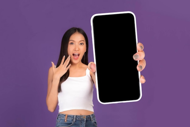 Ritratto di foto a figura intera di bella giovane donna asiatica Ragazza sorpresa eccitata che mostra un grande smartphone con schermo bianco a schermo vuoto isolato su sfondo viola Mock Up Image